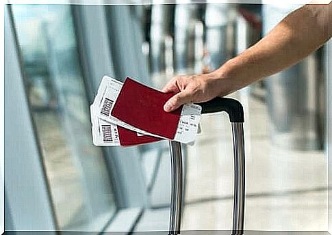 A person walking through an airport with a suitcase and two passports in hand.